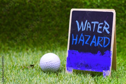 Water Hazard sign and golf ball are on green grass