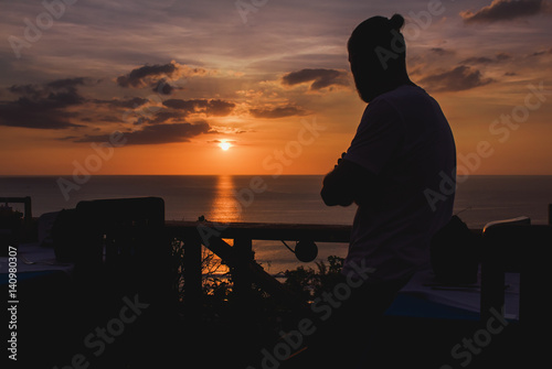 Person looking at sea in the dusk. Silhouette of man standing and looking at the ocean in sunset lights. Horizontal outdoors shot.