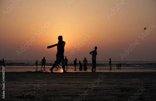 Silhouettes of locals playing beach cricket at sunset in India