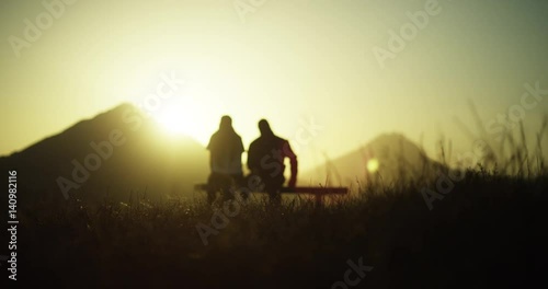 Couple sits on bench at sunset