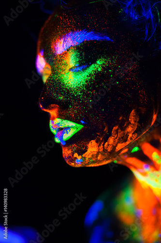 Beautiful extraterrestrial model woman in neon light. It is portrait of beautiful model with fluorescent make-up  Art design of female posing in UV with colorful make up. Isolated on black background