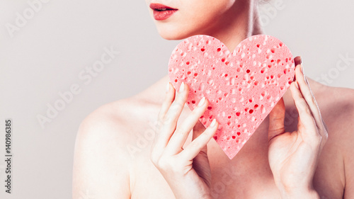 woman holding pink heart sponge in hands.