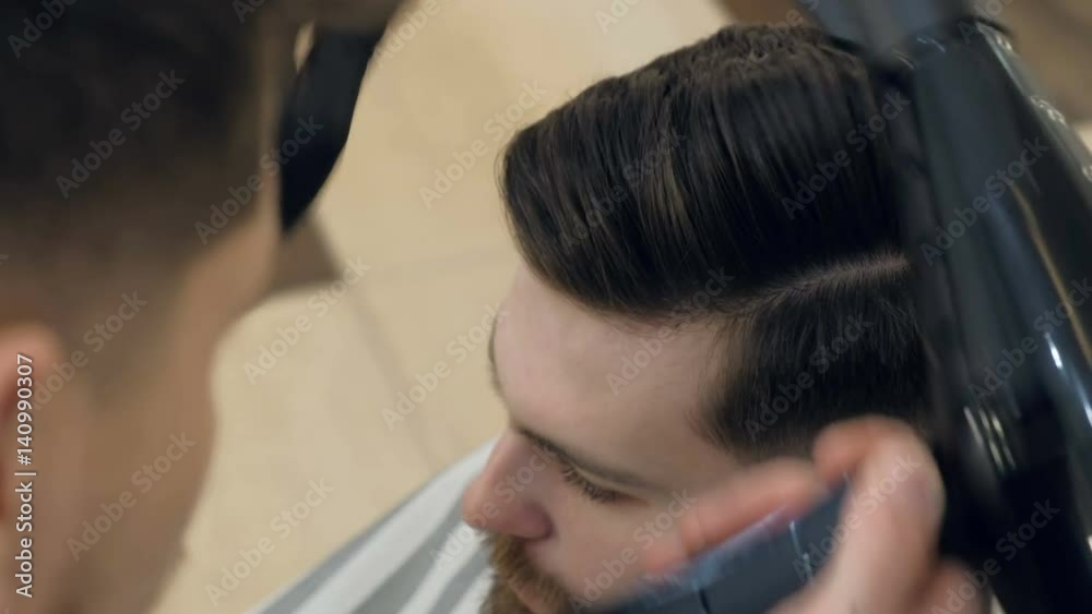 Barber getting groomed at hairdresser with hair dryer while sitting in chair at barbershop Barber getting groomed at hairdresser with hair dryer while sitting in chair at barbershop
