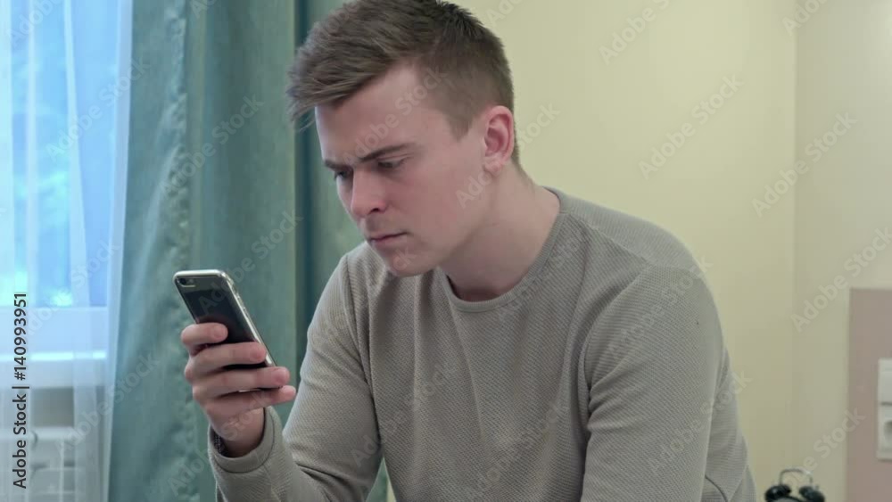Handsome man looks shocked and worried while checking news on smartphone Handsome man looks shocked and worried while checking news on smartphone