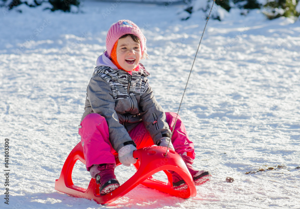 Toddler girl in winter suit on sleigh having fun