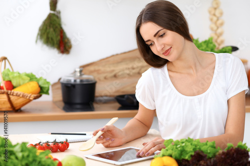 Beautiful Hispanic woman is making online shopping by tablet computer and credit card or searching internet for a new recipe. What to cook for a dinner?