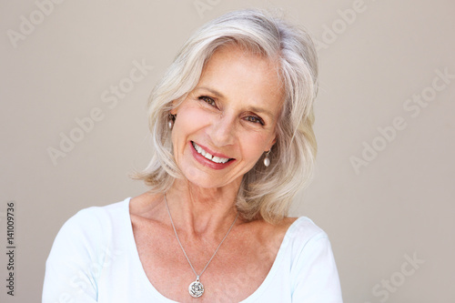 beautiful older woman smiling and standing by wall