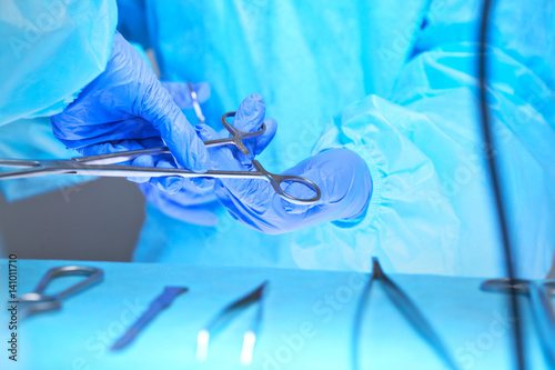 Close-up of of surgeons hands at work in operating theater toned in blue. Medical team performing operation