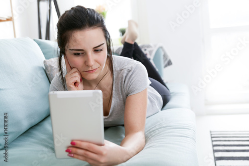 Young woman using pc tablet while lying on comfortable sofa