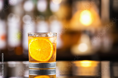 Closeup glass of godfather cocktail with slice of orange and ice cubes at bright bar background. photo