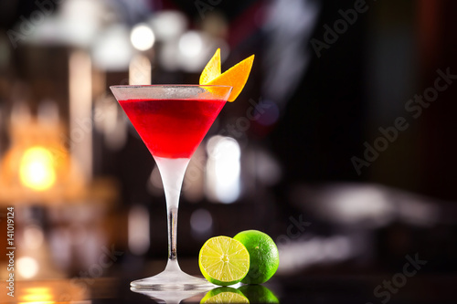 Closeup glass of cosmopolitan cocktail decorated with orange at bar background.