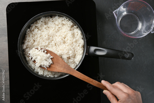 Woman cooking rice in saucepan on stove photo