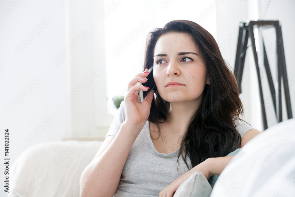 Unhappy worried woman talking on phone while sitting on sofa Unhappy worried woman talking on phone while sitting on sofa