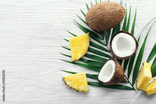 Composition of fresh pineapple slices and coconuts on light wooden background