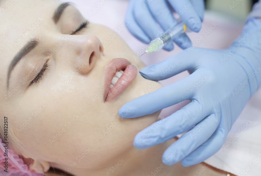 Hands of cosmetologist making injection in face, lips. Young woman gets beauty facial injections in salon. Face aging, rejuvenation and hydration procedures. Aesthetic cosmetology. Close up. Hands of cosmetologist making injection in face, lips. Young woman gets beauty facial injections in salon. Face aging, rejuvenation and hydration procedures. Aesthetic cosmetology. Close up.