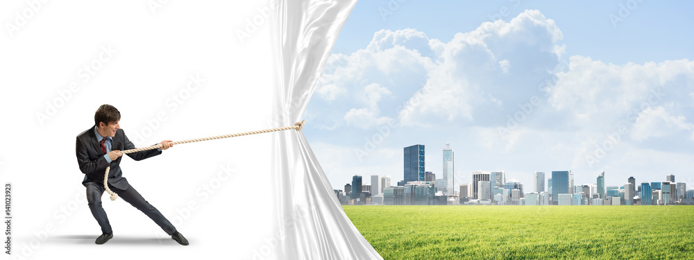 Young man opening white curtain and presenting modern city landscape