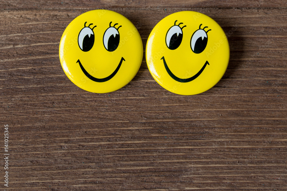 Naklejka Two yellow buttons with smiley faces on a wooden background. Close up