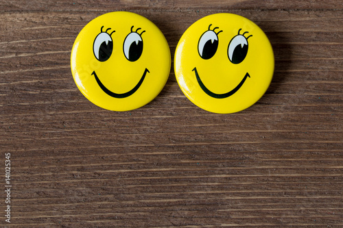 Two yellow buttons with smiley faces on a wooden background. Close up