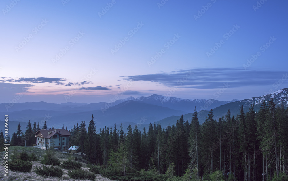 House at a mountain hill at sunrise. Hut in a forest with view at a mountain range at sunrise