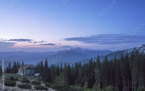 House at a mountain hill at sunrise. Hut in a forest with view at a mountain range at sunrise