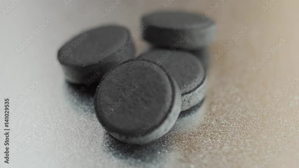 Closed up Activated charcoal carbon pills turning on a metal background. Slow motion. Closed up Activated charcoal carbon pills turning on a metal background. Slow motion.