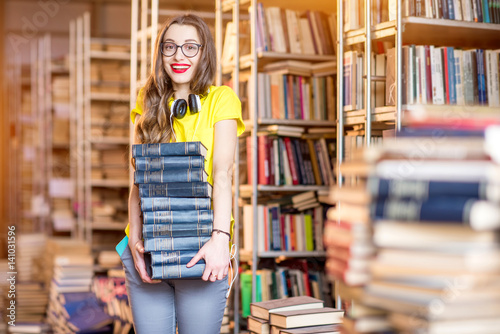 Portrait of young happy woman carrying a heap of books at the old library