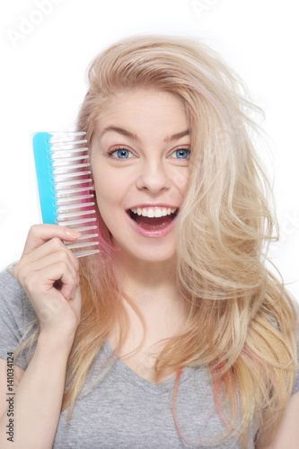 Emotional portrait of young beautiful excited blond girl with hair comb in her hand