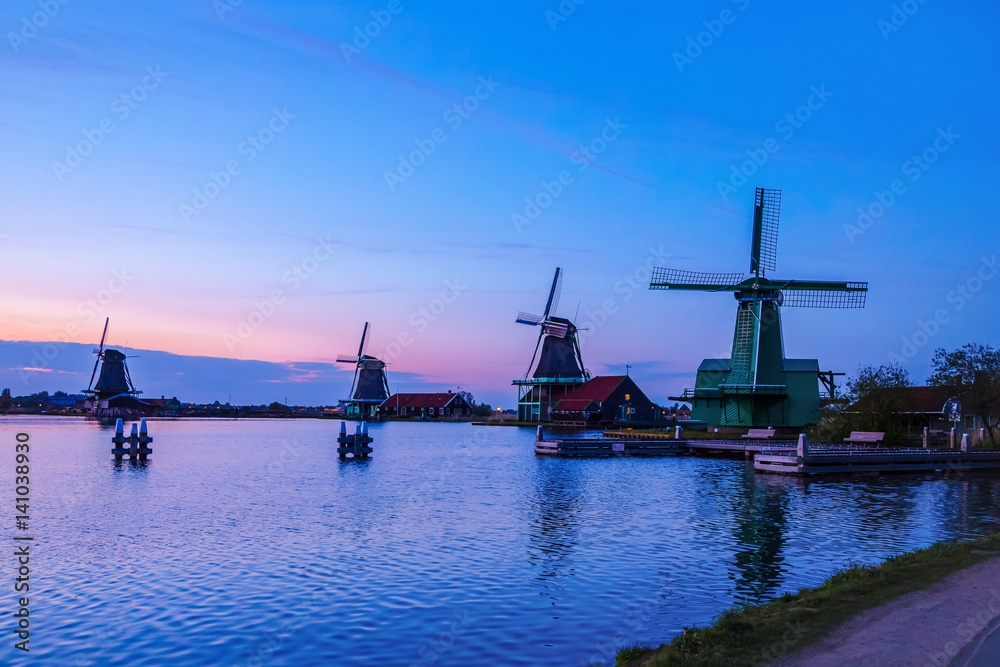 Dutch mill by evening. Sunset in landscape with mill the Netherlands. Dutch windmill at sunset at a lake. River Zaan with four windmills lined up at 'De Zaanse Schans' in Zaandam, Netherlands