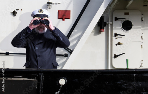 Kapitän steht mit Fernglas an der Reeling