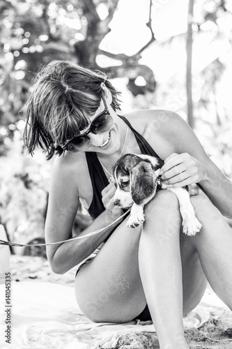Young attractive girl with her pet dog Beagle at the beach of tropical island Bali, Indonesia. Happy moments. Black and white photo.
