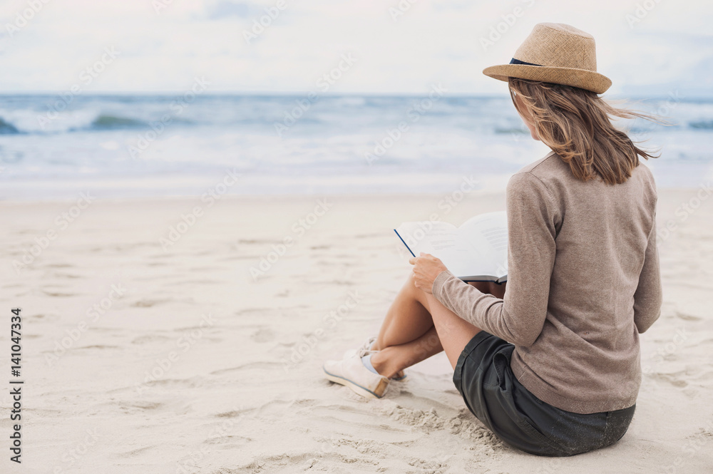 Young woman reading a book on the beach. Relaxation resting vacations concept