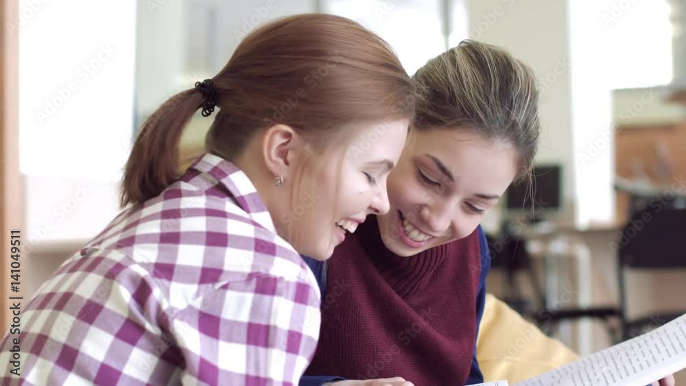 Portrait of two smiling girls in library looking into magazine Portrait of two smiling girls in library looking into magazine