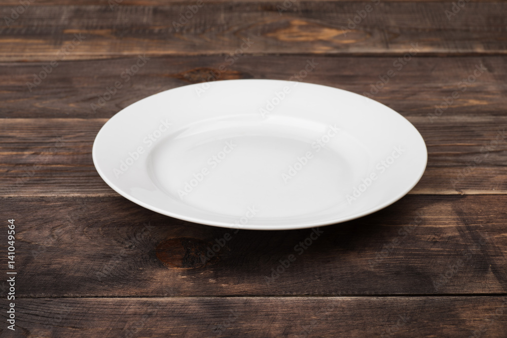 White empty plate on dark wooden table White empty plate on dark wooden table