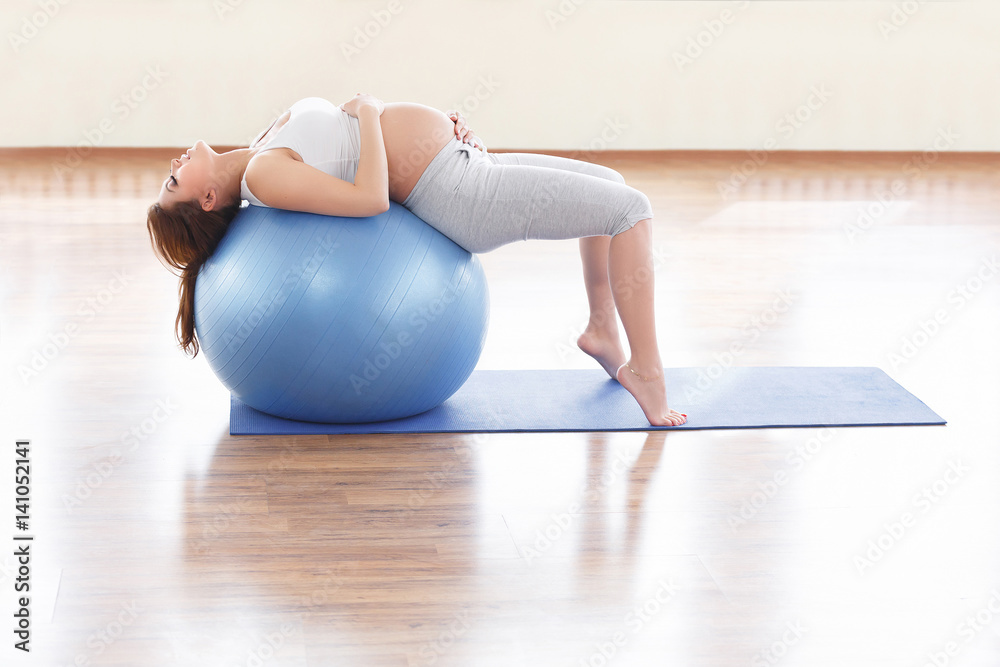 Naklejka premium Portrait of a beautiful young pregnant woman executing exercises with fitball