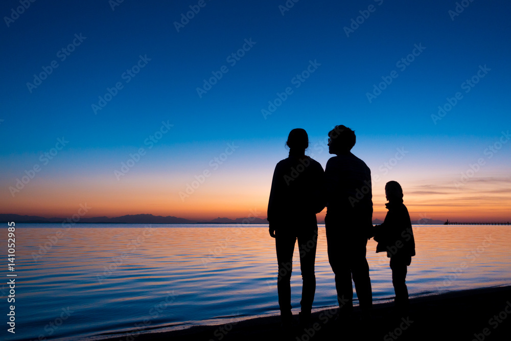 silhouette of three people standing on the beach in sunrise