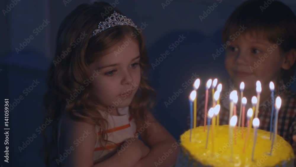 A little girl looks at candles on a festive cake and makes a wish in Slow motion A little girl looks at candles on a festive cake and makes a wish in Slow motion