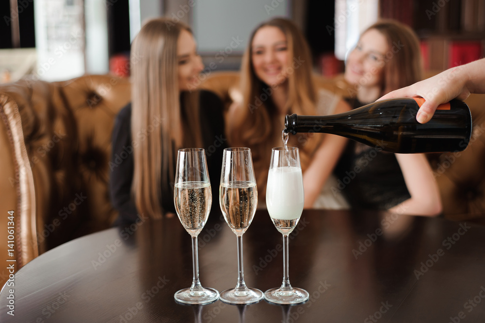 Man fills glasses of champagne for three beautiful young women in restaurant