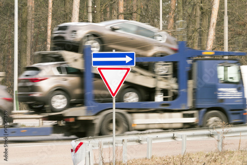 Truck with new cars on the road with road sign "Give Way"