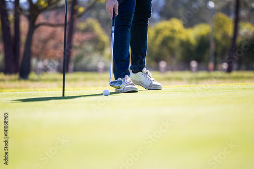 Close up view of a golfer just pushing in a golf ball into the hole on a green