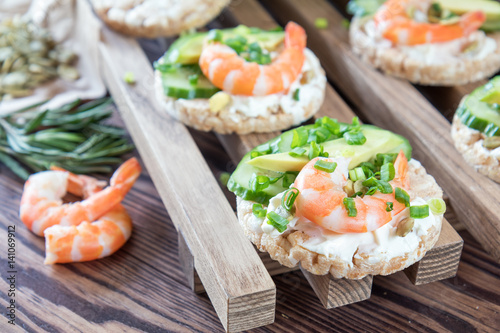 Rice cakes with sliced avocado cucumber shrimp and cream cheese. Fresh parsley and rosemary. Vegetarian, vegan concept. Shallow depth of field. Coloring and processing photo.