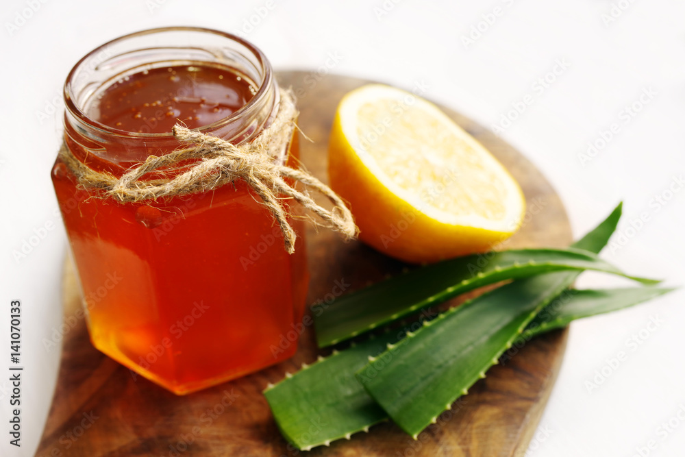 Honey in a glass jar, lemon and aloe vera on a wooden board on a white background. Alternative medicine