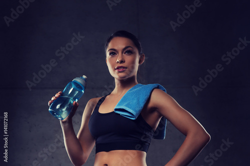 woman with towel drinking water from bottle in gym