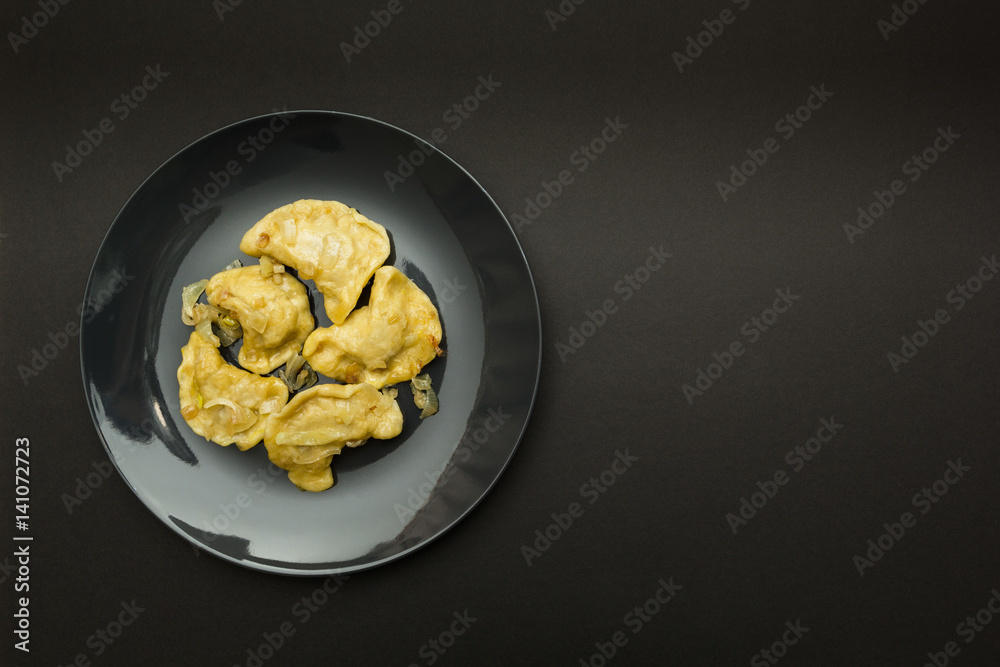 Black plate with pierogies on a black background. Place for the text. Black plate with pierogies on a black background. Place for the text.