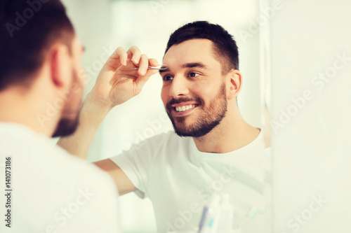 man with tweezers tweezing eyebrow at bathroom