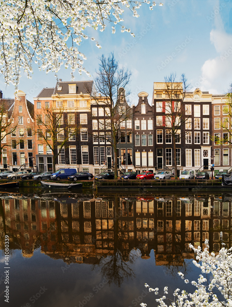Facades of dutch houses over canal with mirror reflections at blooming, Amsterdam, Netherlands