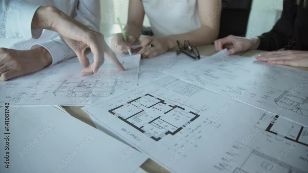 Close up hands of three workers discussing building drawings in office. Closeup shooting of arms moving pictures, watching attentively on images. design drafts for construction of large sports complex