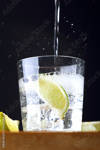 Glass of gin tonic with lime and tonic falling