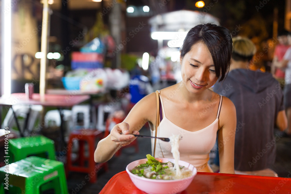 Woman enjoy her bowl of noodles in outdoor night market in Bangkok city