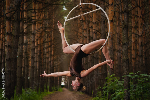 Beautiful and graceful aerial gymnast performs exercises on the air ring in the woods photo