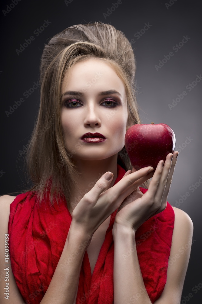 portrait of the young woman in a red scarf with a vanguard hairstyle which holds in hand red apple on a gray background portrait of the young woman in a red scarf with a vanguard hairstyle which holds in hand red apple on a gray background